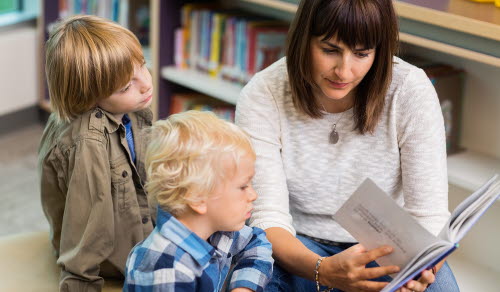 Young teacher reading book for students in school library