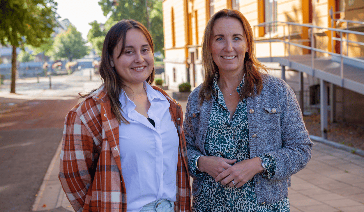 Två kvinnor som står bredvid varandra framför en gul byggnad.