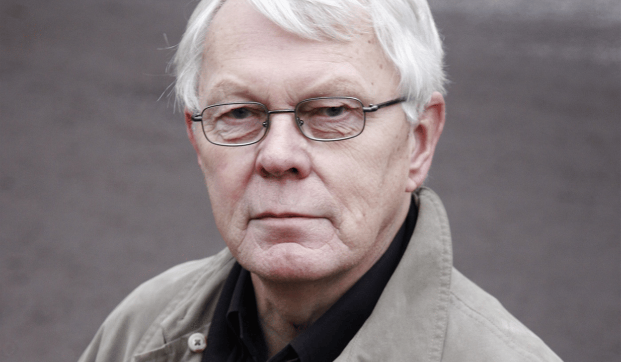 En man med vitt hår som bär en trenchcoat.