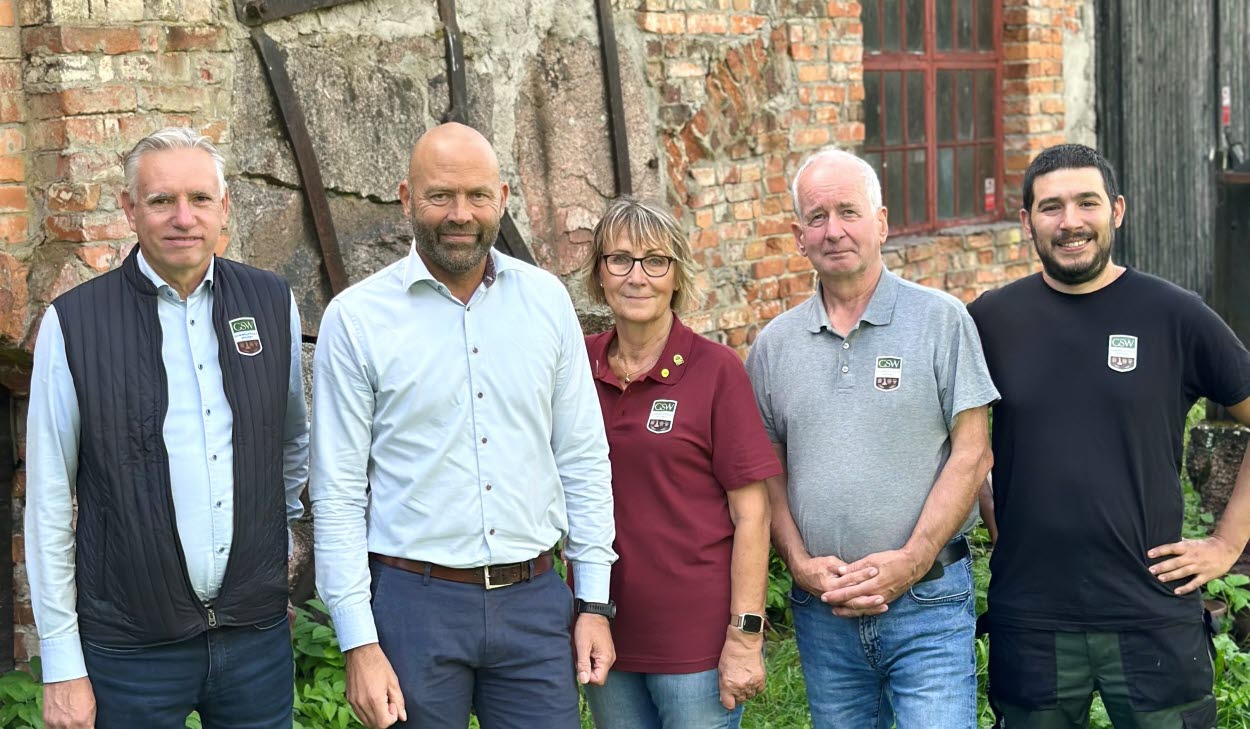 Fem personer står i helkroppsfigur framför en gammal tegelbyggnad.