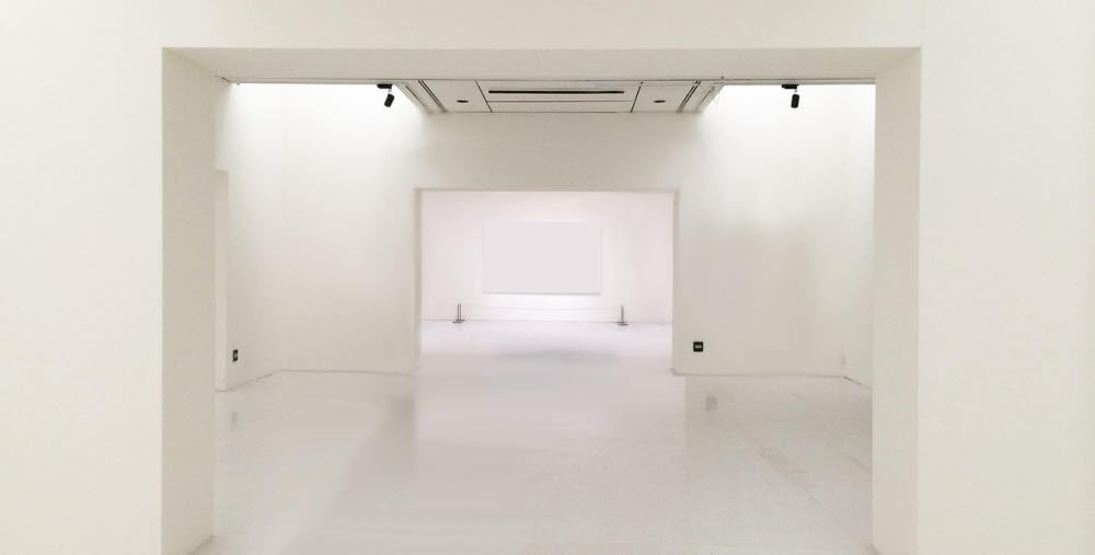Tomt utställningsrum med vita väggar, tak och golv i flera öppna sektioner.