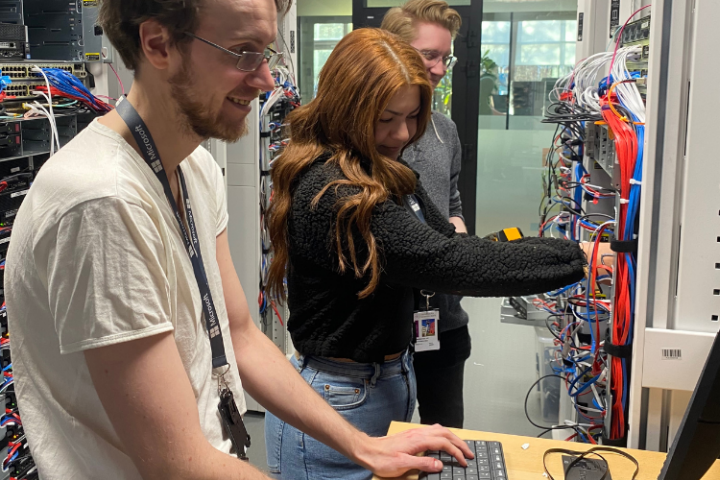 Tre personer arbetar vid servrar och kablage i en datahall.