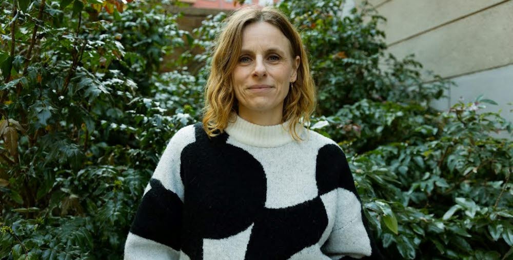 Person ståendes framför en grön buske iklädd en svart och vit mönstrad tröja.