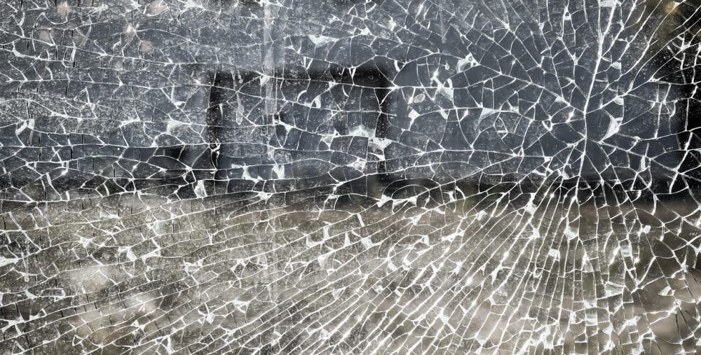 Närbild av ett splitterkrossat fönster med spindelnätsliknande sprickmönster.