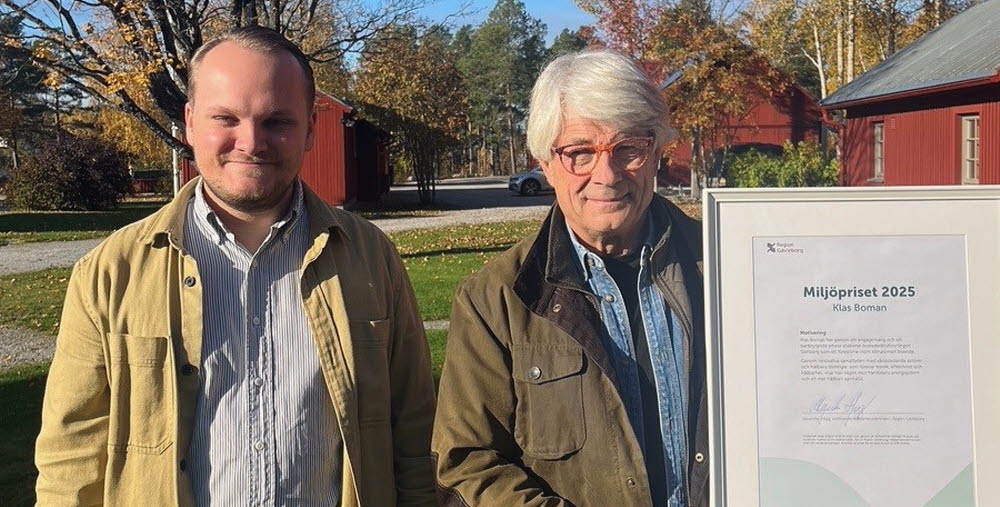 Två män står bredvid varandra i utomhusmiljö på hösten. Den ena håller i ett inramat diplom för Miljöpriset 2025.