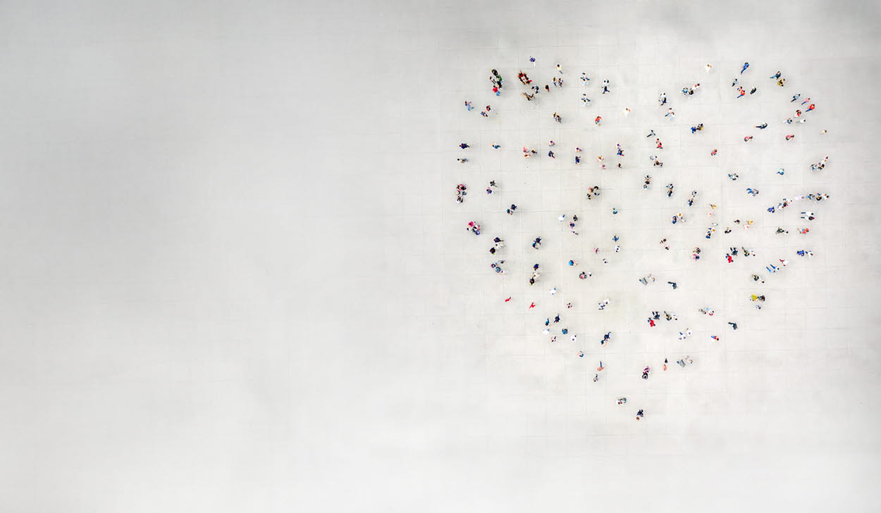 Människor står utspridda så att de tillsammans bildar formen av ett hjärta på en stor öppen yta, sedd uppifrån.